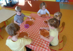 Piątka dzieci stempluje gąbką talerzyk papierowy na brązowo.